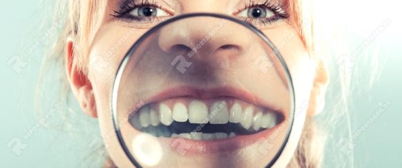 Happy young woman showing white teeth through magnifying glass. 
